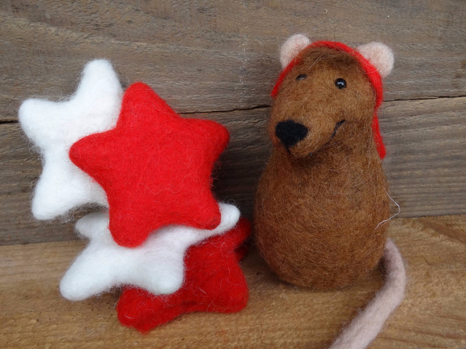 Braune gefilzte Maus mit Weihnachtsmütze und einigen bunten Weihnachtssternen