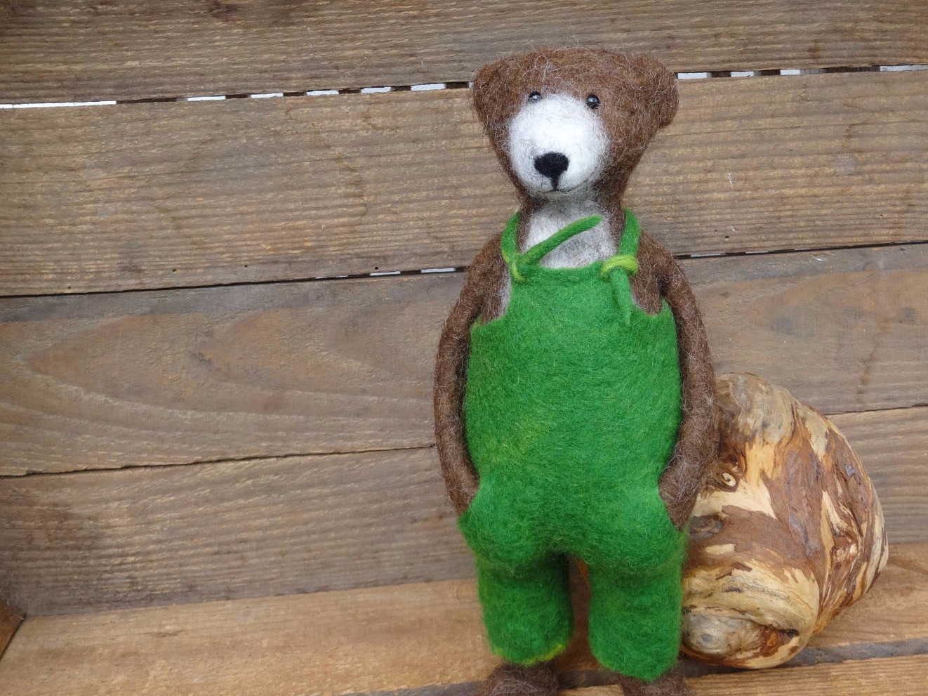 Gefilzter Bär mit grüner Latzhose in einer Holzkiste