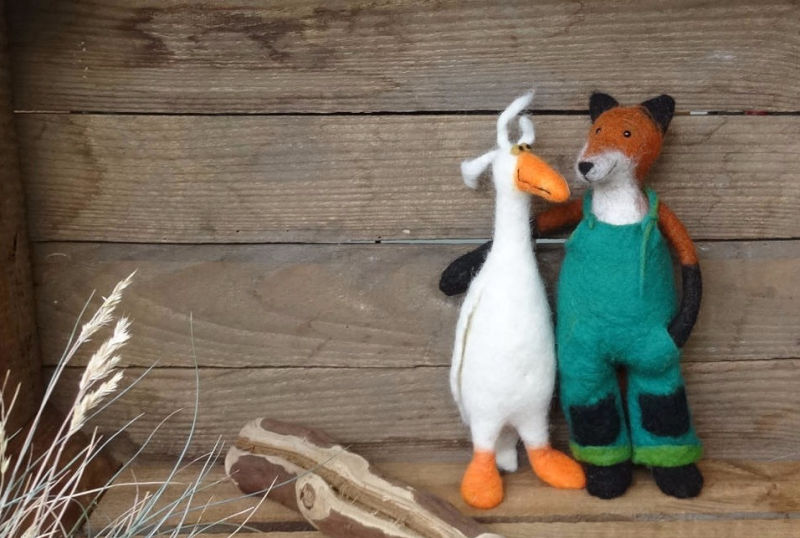 Ein gefilzter Fuchs mit Latzhose und eine gefilzte weiße Gans stehen nebenenander.